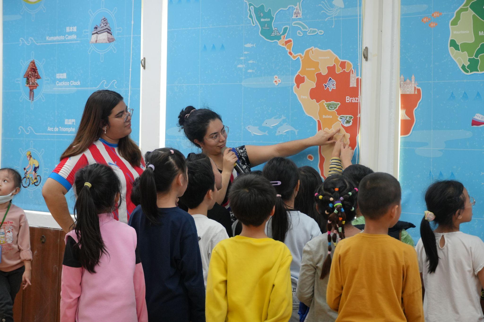 Paraguayan participants Luana Vallejos and Ingrid Pereira show students the location of Paraguay on a world map, sparking curiosity and questions among the children. (Photo credit: ICI)